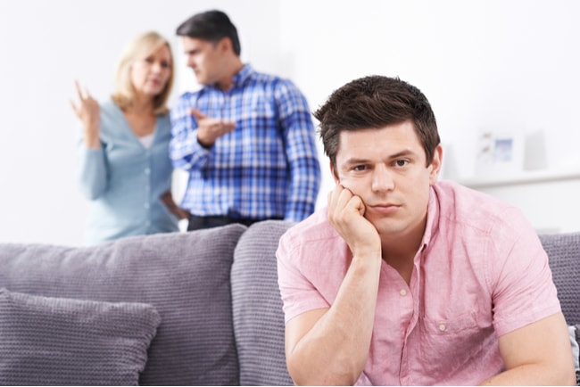ung vuxen man i soffa med diskuterande föräldrar i bakgrunden