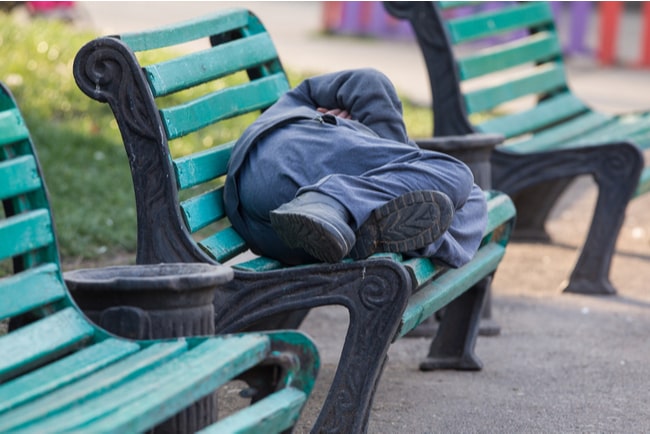 En man i blå byxor ligger på en grön parkbänk och sover.