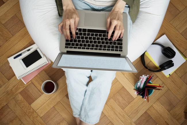 Kvinna med laptop i knät och kontorsmaterial på golvet bredvid.